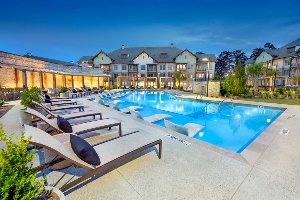Resort-style pool lit at dusk, lined with lounge chairs, beside the clubhouse at Town Kennesaw apartments in Kennesaw, GA.