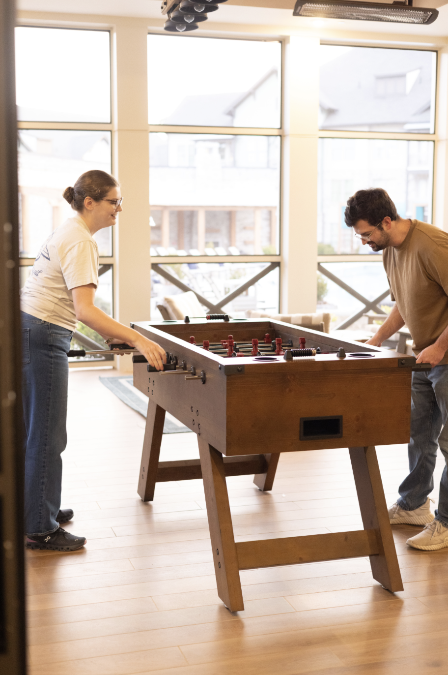 Two residents playing foosball in the sunlit resident clubroom at Town Kennesaw luxury apartments in Kennesaw, GA